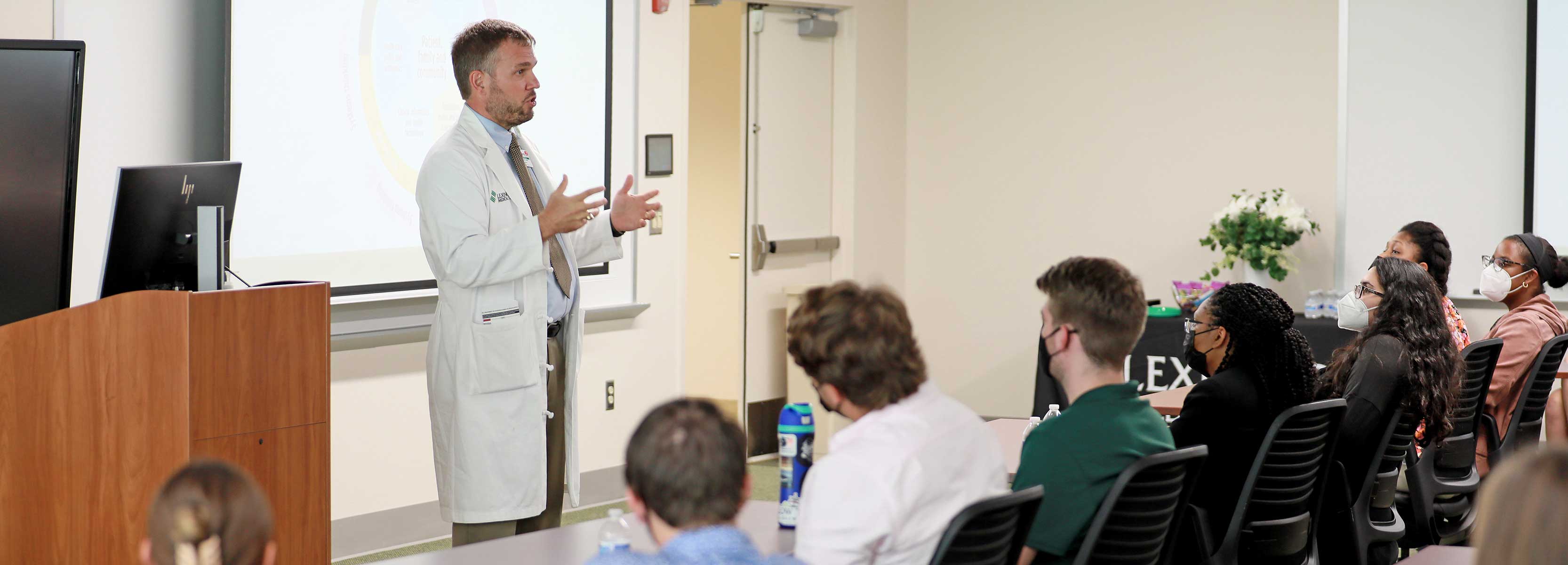 Dr. Brent Powers speaking to a class in front of a slideshow.